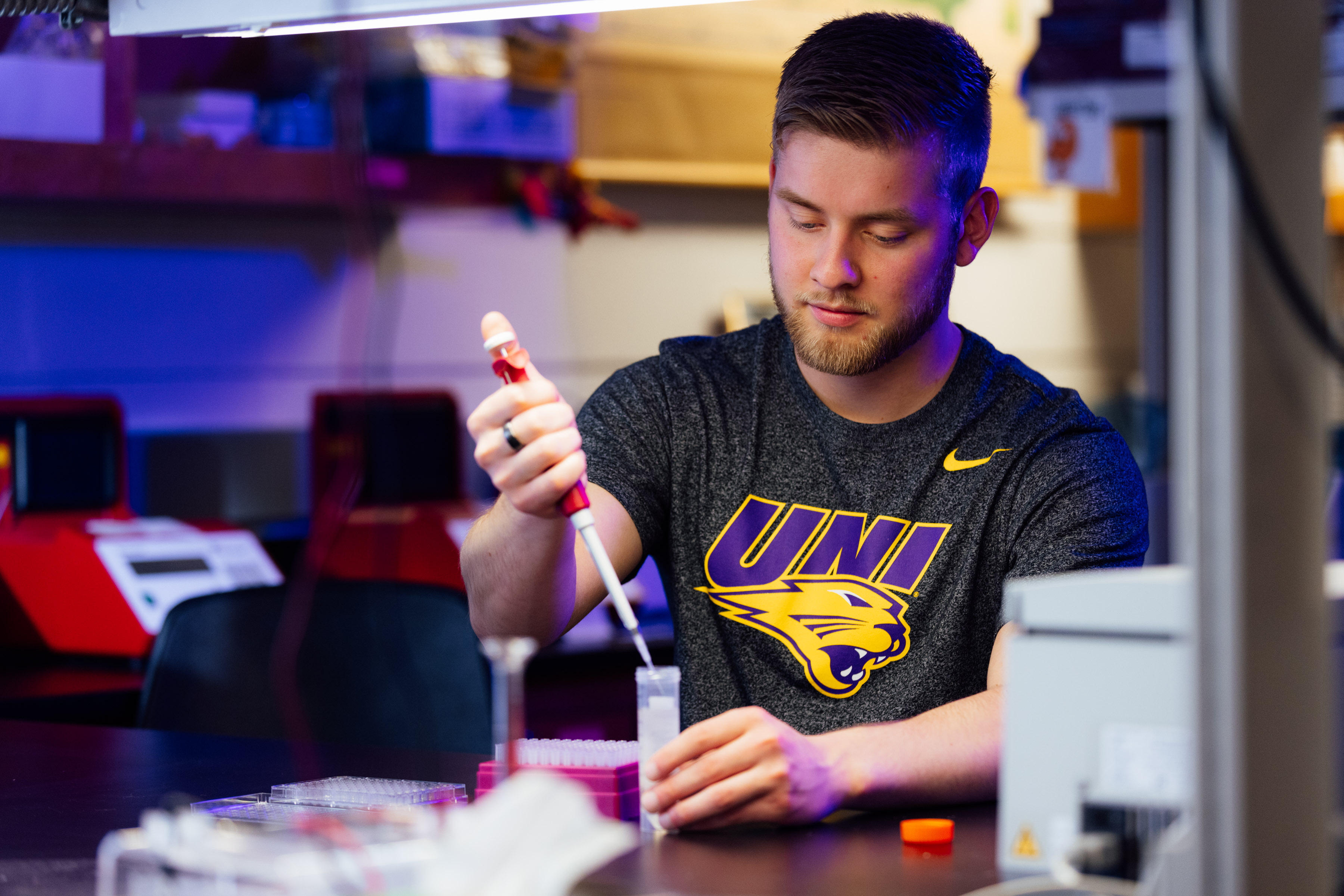 UNI biology student using a syringe with liquid in a bottle.