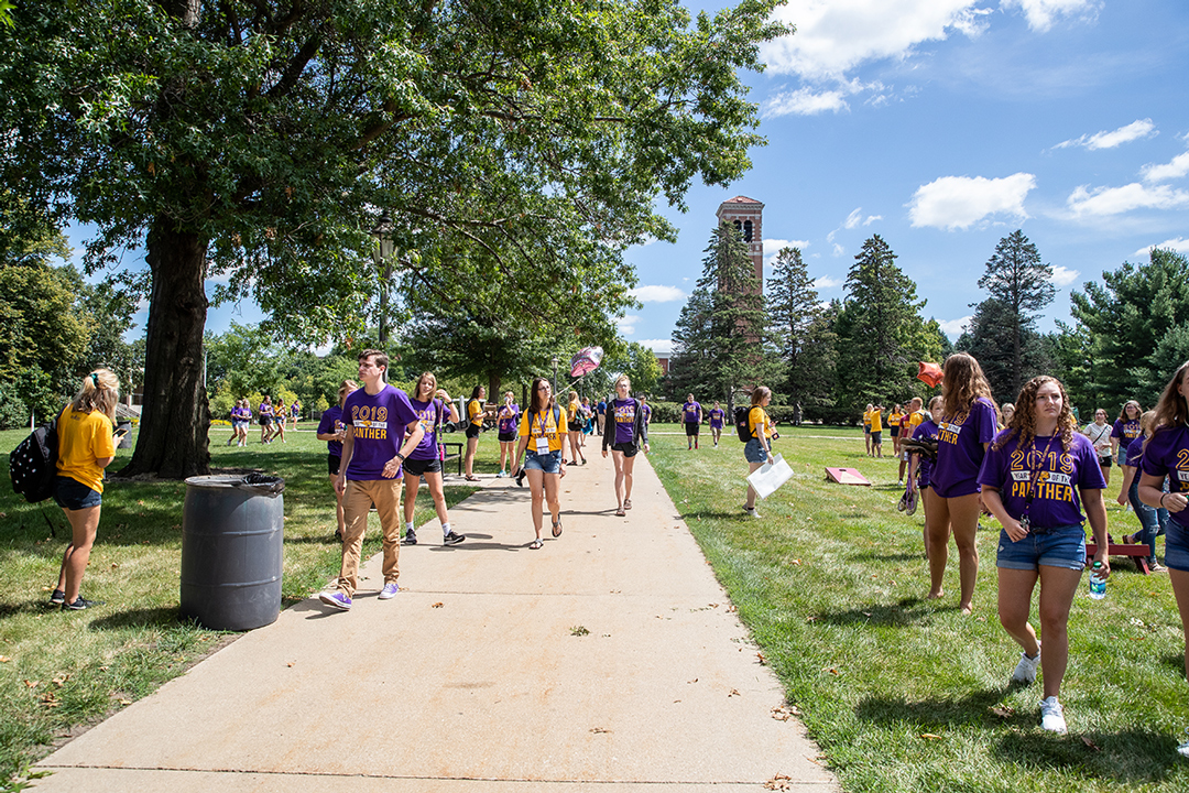 a large group of UNI students wearing purple and gold walking by the Campanile
