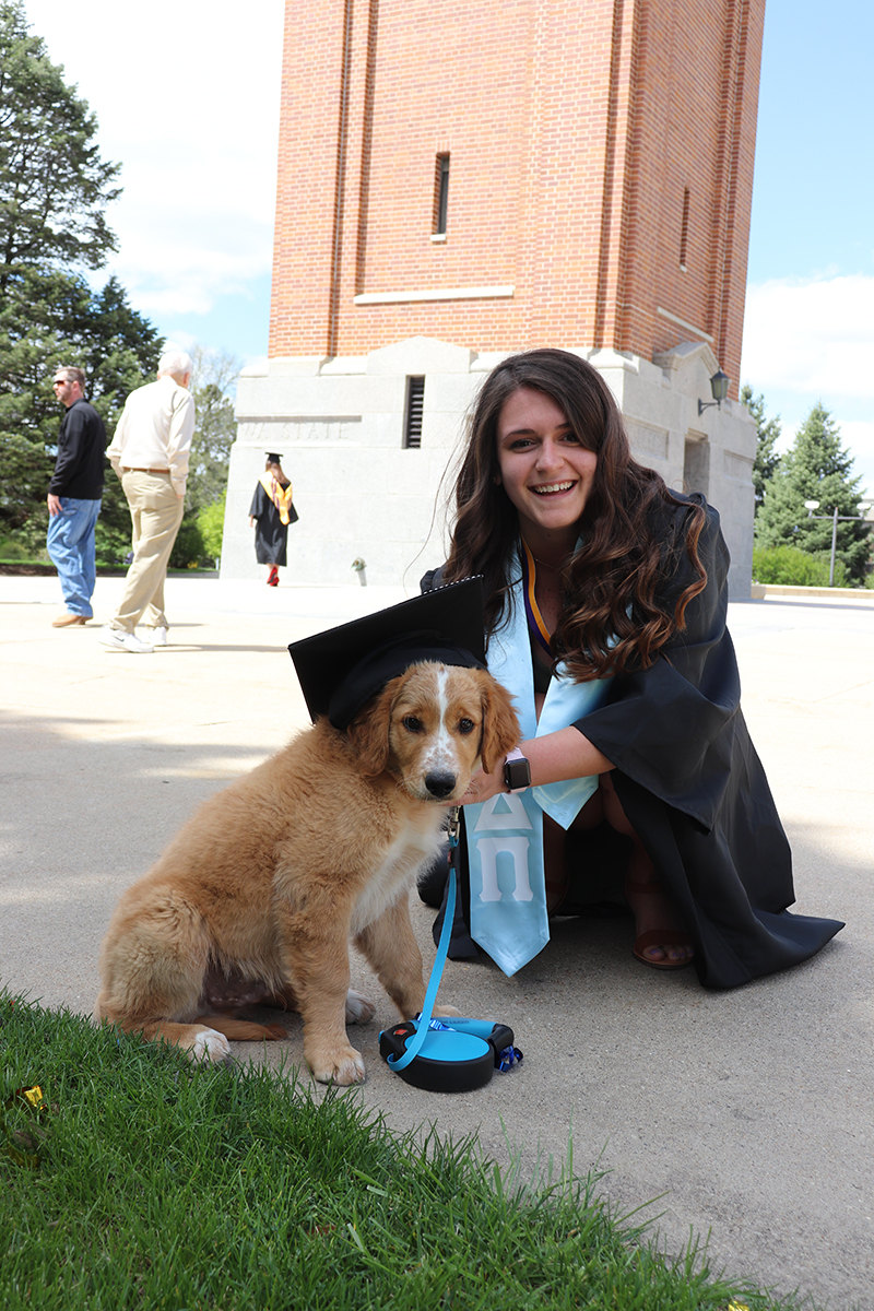 UNI student in graduation gown posing with her puppy wearing her graduation cap