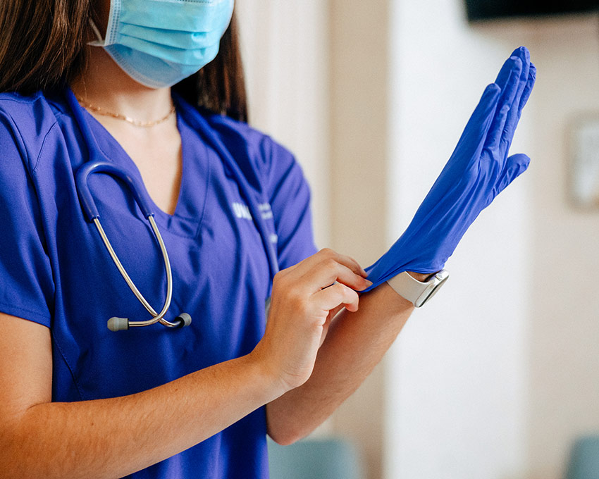 UNI Nursing student wearing purple scrubs putting on a purple glove