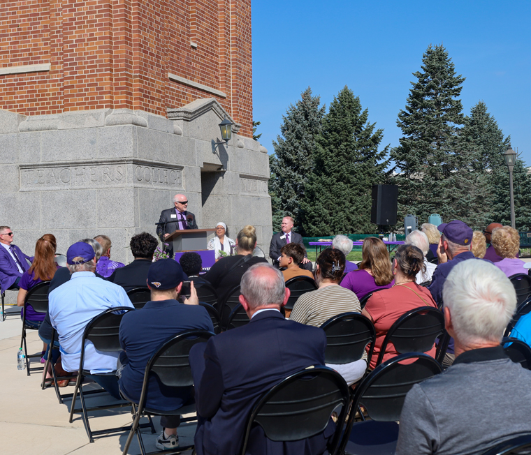Dave Takes speaks behind a podium on the Campanile Plaza