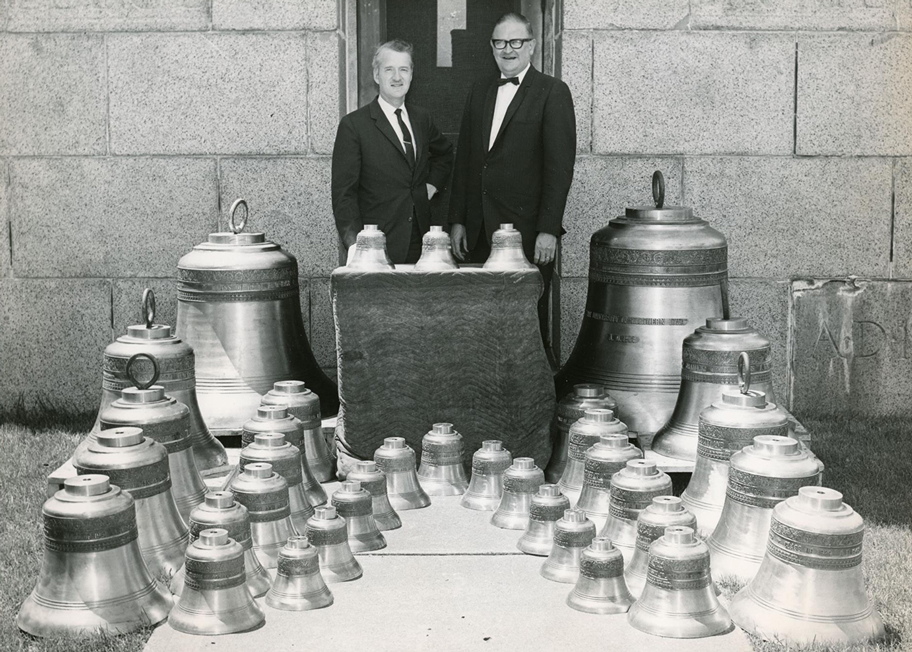 two men standing with the 32 bells that are to be added to the Campanile