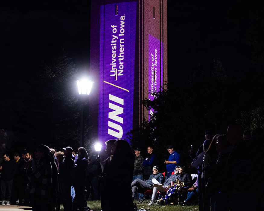 the UNI Campanile at night surrounded by people for the Our Tomorrow campaign launch-UNI logos and colors are projected onto the sides of the Campanile