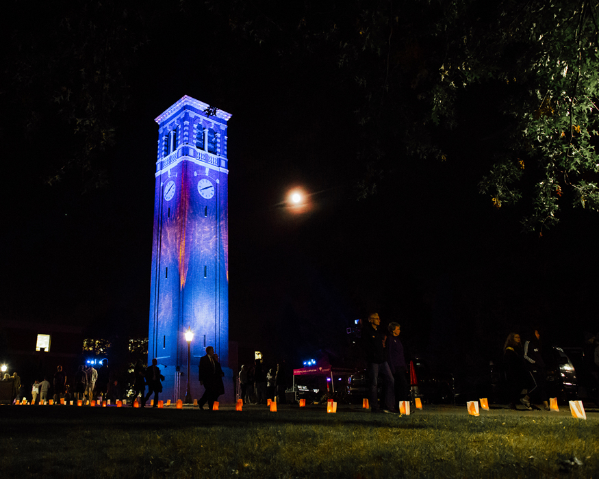 people walking at night towards the Campanile as blues and purples are projected onto the Campanile