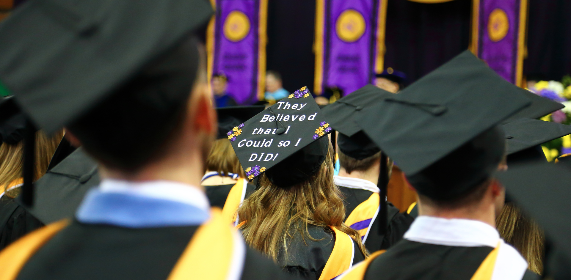 UNI students at commenement with a mortar board visible reading, "They believed that I could so I did!"