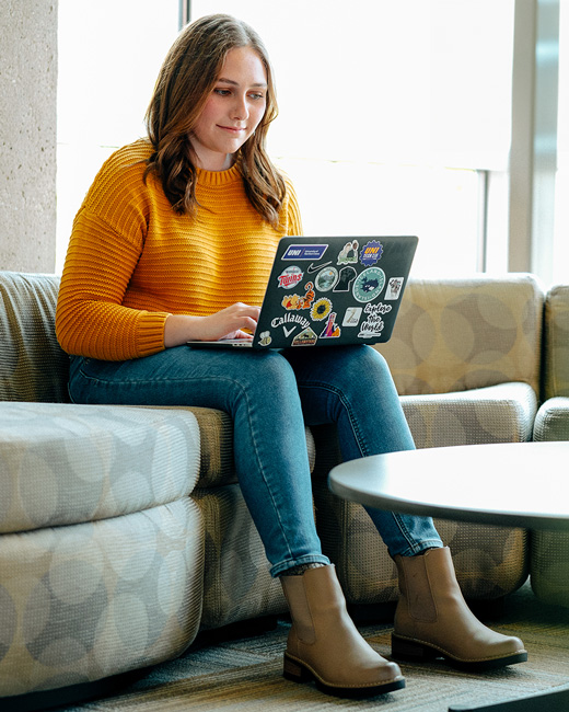 UNI student in a yellow sweater studying on their laptop computer