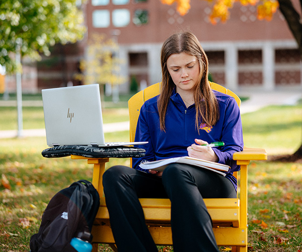 A student studying outdoors in a yellow chair on UNI's campus