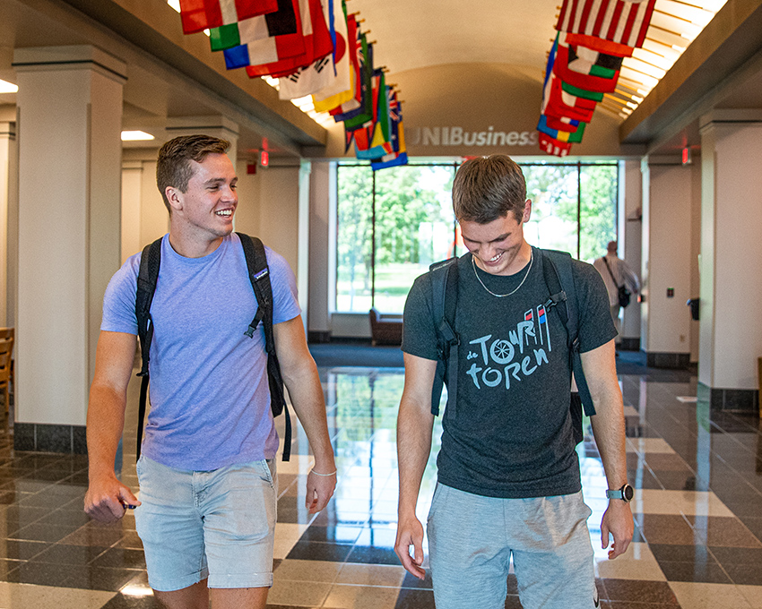 Two UNI students walking through the Hall of Flags in Curris Business Building