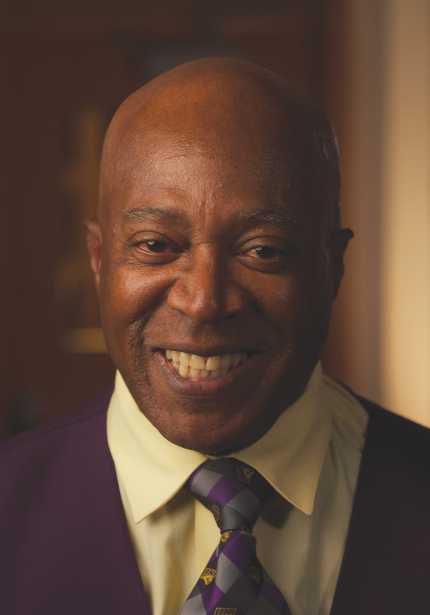 Black man with a suit and tie smiling at the camera.