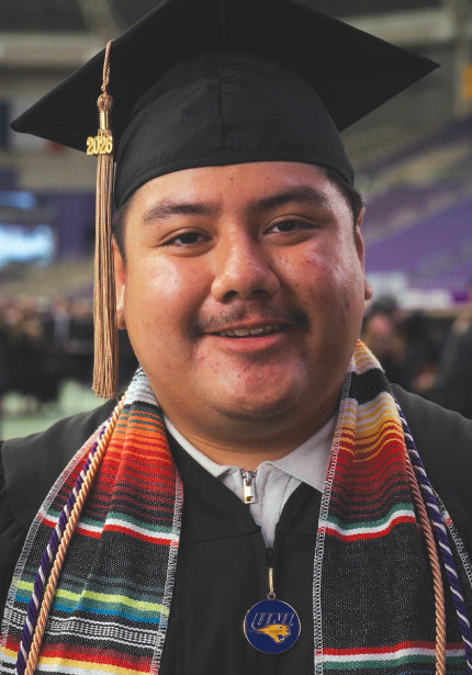 UNI student with black cap and gown and a multicolored stole.