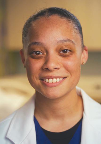 UNI female nursing student with a white coat smiling at the camera.